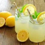 Two mason jar glasses of homemade lemonade on a rustic wooden background